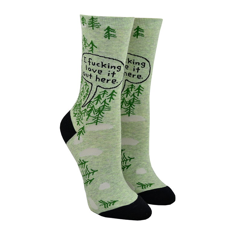 Shown on leg forms, a pair of women's Blue Q brand combed cotton crew socks in green with a black heel and toe. The socks feature a cartoon-y pine tree motif all over the sock with the words, 