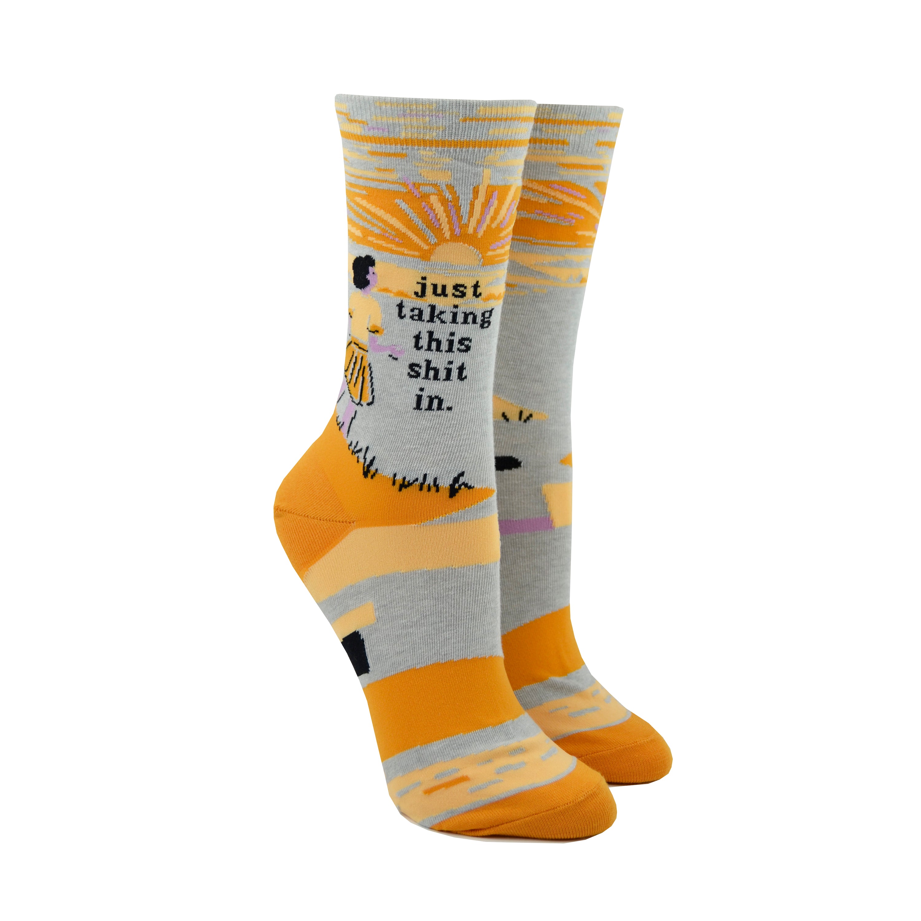 Shown on leg forms, a pair of light grey socks with an orange heel and toe. These socks feature a cartoon woman watching the sunset with the phrase, 