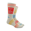 Shown on a leg form, a pair of Blue Q cream-white cotton men’s crew socks with orange abstract winking face, “Still Got It” text and abstract accent lines in blue, orange, and yellow