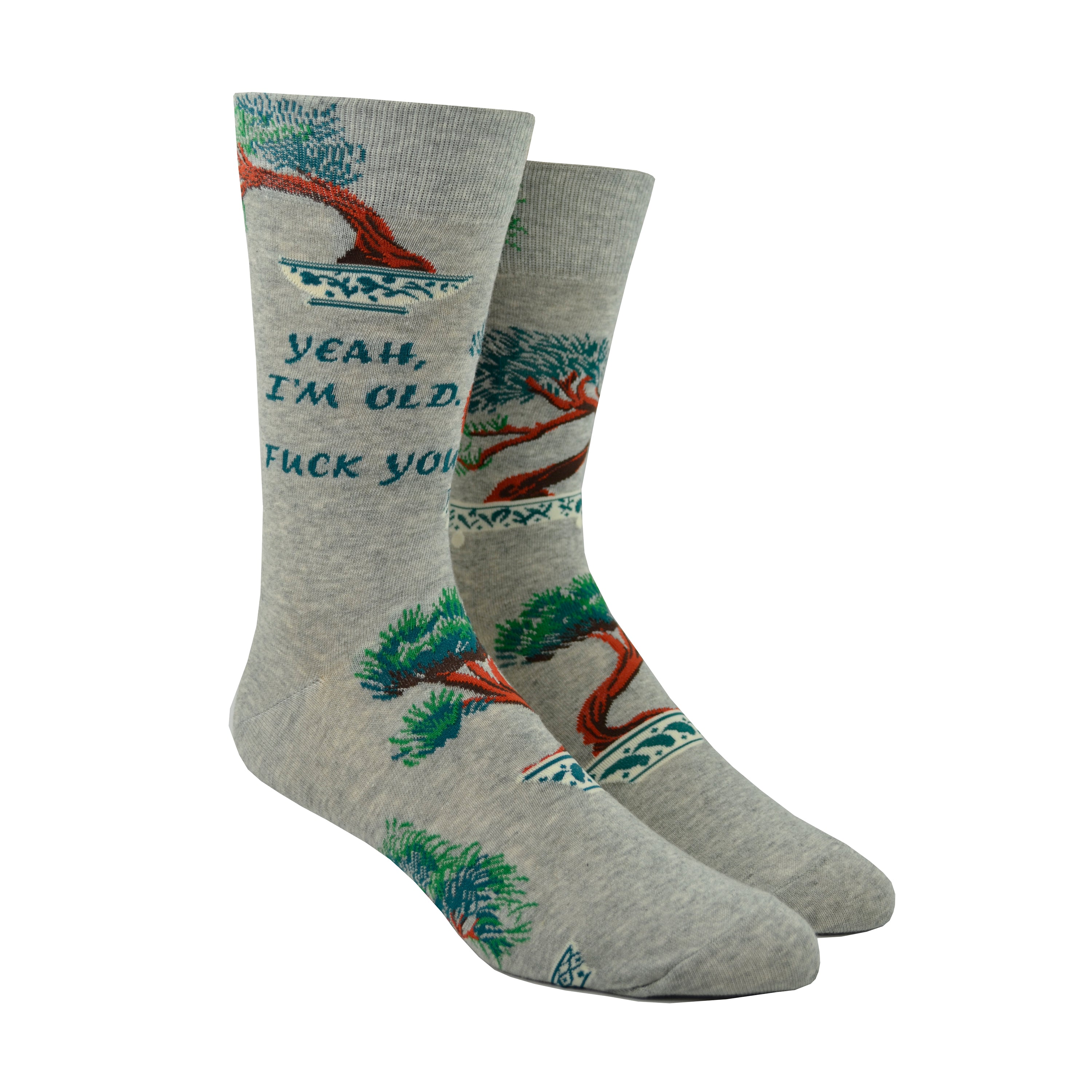 Shown on leg forms, a pair of Blue Q brand men's cotton crew sock in grey with bonsai trees scattered around the sock. The text on the leg of the sock reads, 