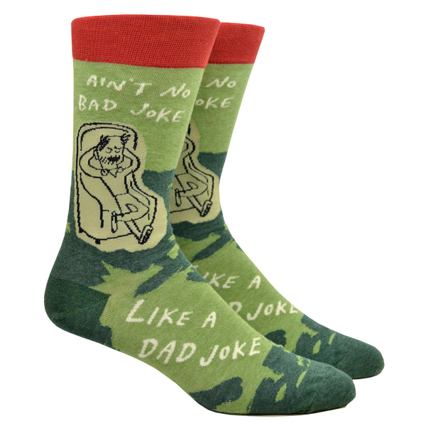 Shown on a leg form, a pair of Blue Q green and brown cotton men’s crew socks with a dad relaxing on a chair and the words “Ain’t no Bad Joke Like a Dad Joke”