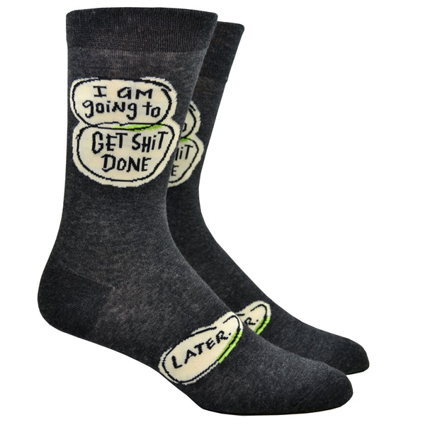 Shown on a leg form, these dark gray cotton funny men's crew socks by the brand Blue Q have word bubbles with the words "I am going to get shit done" on the leg and another word bubble with the word "later" on the foot.