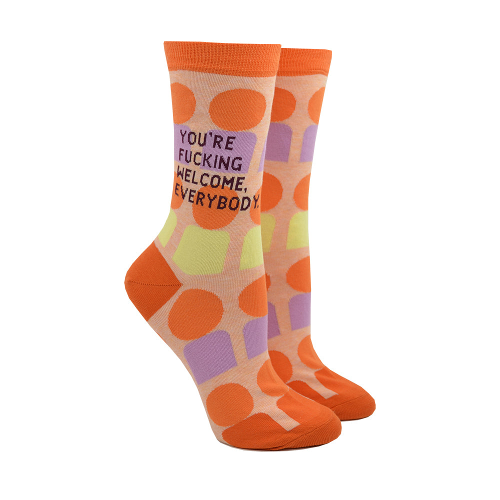 Shown on leg forms, A pair of orange socks that have a retro geometric pattern in orange, lilac and, yellow. The socks have text that reads, 