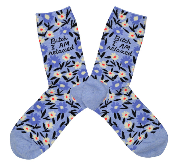 Shown in a flatlay, a pair of Blue Q blue cotton women’s crew socks with blue and white floral pattern and “Bitch, I AM relaxed” text