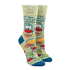 Shown on leg forms, a pair of women's Blue Q cotton crew socks in olive green with a blue heel and toe. These socks feature a cartoon women over a pot with a spoon and the phrase, "Get the hell out of My kitchen" above her. The foot of the sock features abstracted pots and pans in red, green, and orange.