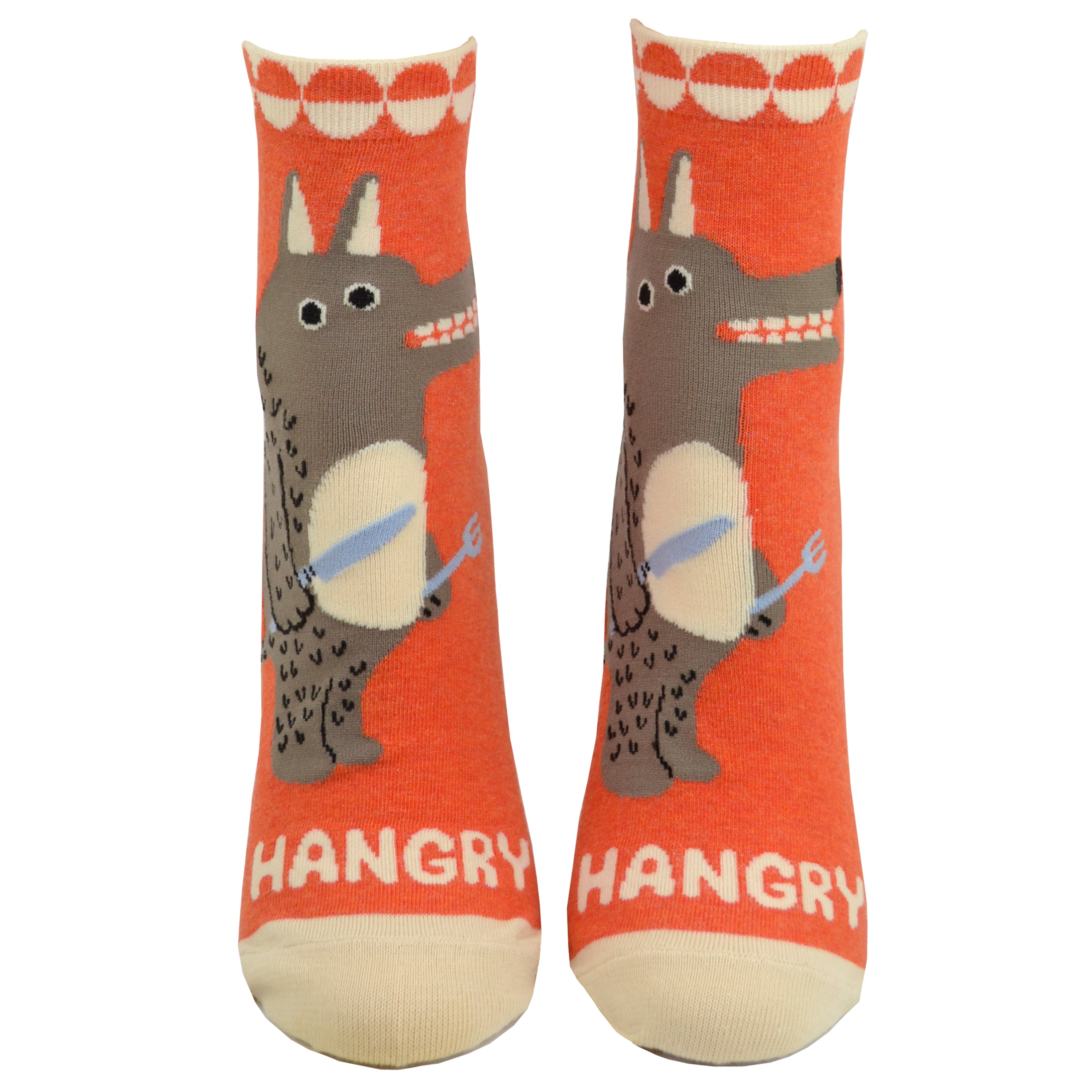 Shown on foot forms from the front, a pair of women's Blue Q cotton ankle socks in orange with a cream heel, toe, and cuff. The front of the socks features a cartoon wolf man with a knife and fork and the word 