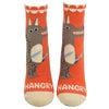 Shown on foot forms from the front, a pair of women's Blue Q cotton ankle socks in orange with a cream heel, toe, and cuff. The front of the socks features a cartoon wolf man with a knife and fork and the word "HANGRY" in cream across the toe.