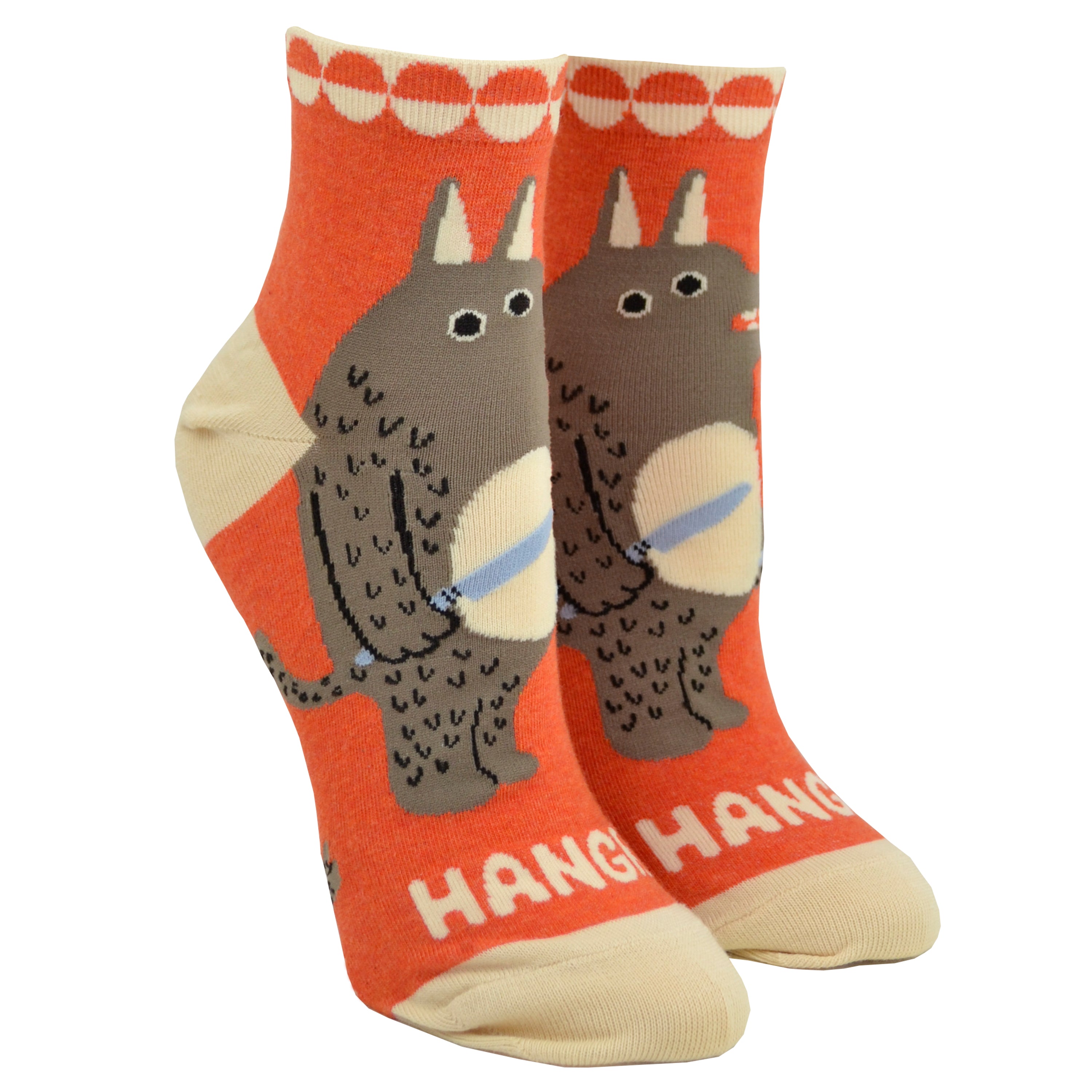 Shown on foot forms from the side, a pair of women's Blue Q cotton ankle socks in orange with a cream heel, toe, and cuff. The front of the socks features a cartoon wolf man with a knife and fork and the word 