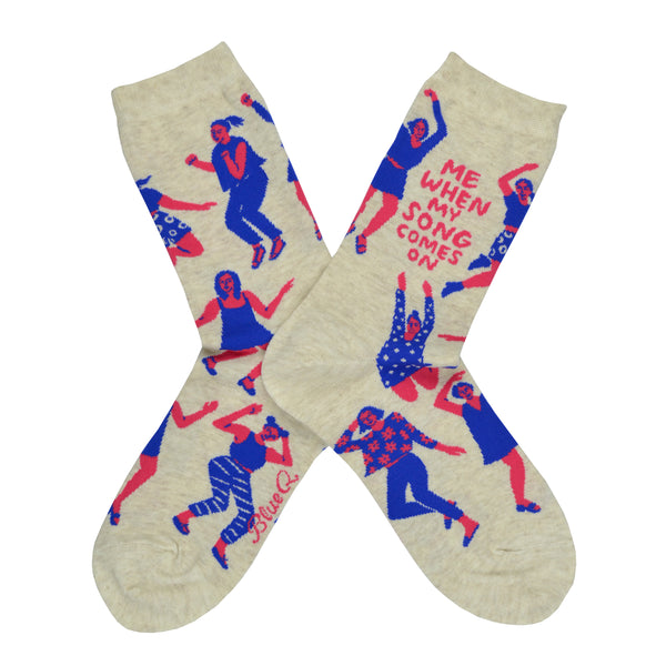 These cream cotton women's novelty crew socks by the brand Blue Q feature pink women wearing purple clothes dancing in different styles and the quote "Me When My Song Comes On".