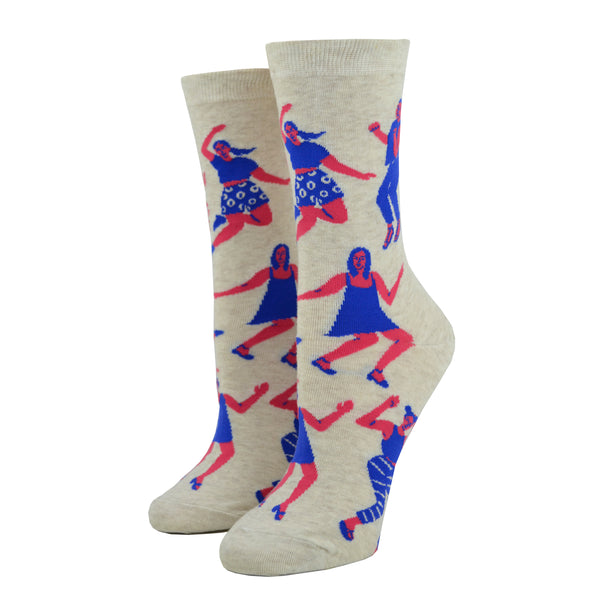 Shown on a leg form, these cream cotton women's novelty crew socks by the brand Blue Q feature pink women wearing purple clothes dancing in different styles.