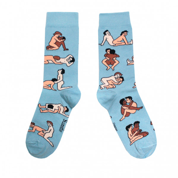 Shown in a flatlay, a pair of women's CouCou Suzette cotton crew socks in light blue with gay male lovers engaging in varying Kama Sutra sex positions all over the socks.