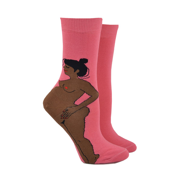 Shown on leg forms, bright pink CouCou Suzette socks with a naked, black pregnant woman. The woman's belly makes the ankle of the sock.