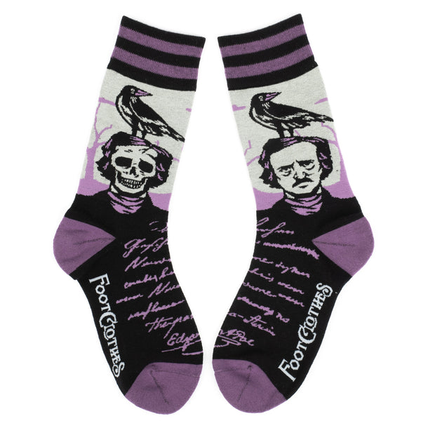Shown in a flatlay, a pair of unisex crew socks in  purple, black, and, gray. The ankle and heel of the socks are purple and the cuff is purple and black stripped. The leg of the socks depicts famous poet, Edgar Allan Poe with a raven on his head and the other side of the sock Edgar with a skull for a face with a raven on his head. The foot of the sock is black with purple script. 