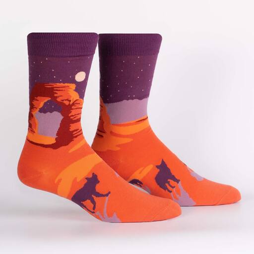A pair of sock it to me crew length cotton socks featuring a nighttime scene from Arches National Park in shades of orange and purple, with coyotes in the foreground