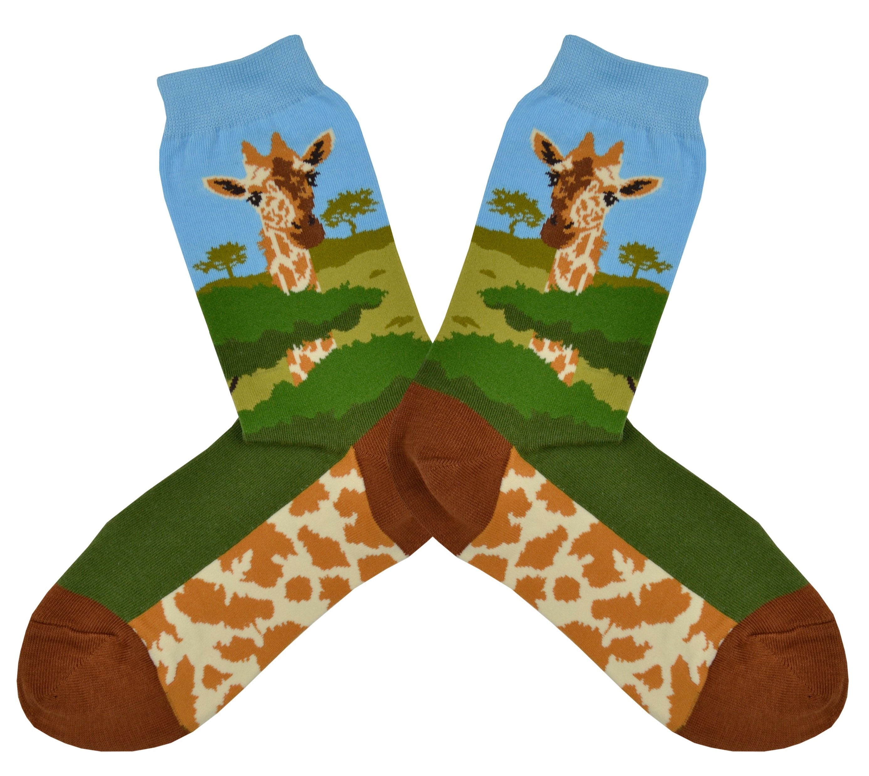 Shown in a flatlay, a pair of women's Foot Traffic brand cotton crew socks with a blue cuff and brown heel and toe. The leg of the sock has a giraffe head and neck with a savanna background. The foot is dark green on the top and the sole is a giraffe pattern.
