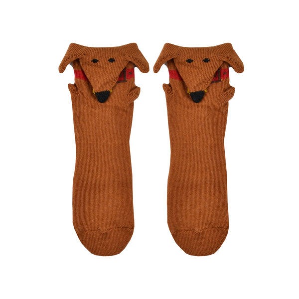 Shown in a flatlay, a pair of Foot Traffic brand kids cotton crew socks in brown. These 3D socks looks just like a wiener dog with little paws, a long nose, and 2 floppy ears at the top of the sock.