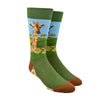 Shown on a foot form, a pair of Foot Traffic green cotton men's crew socks with a giraffe and acacia trees