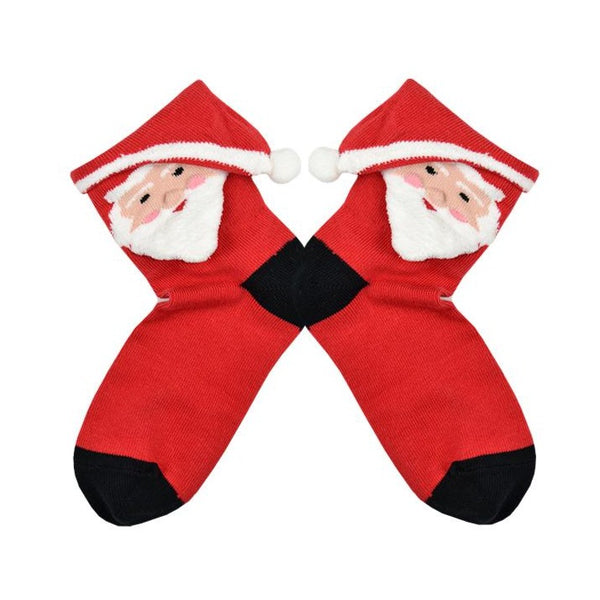 Shown in a flatlay, a pair of Foot Traffic brand women's 3D cotton crew socks in red with a black heel and toe. The top of this sock is a fold over cuff that turns into Santa's hat with a cute Santa face below on the leg.