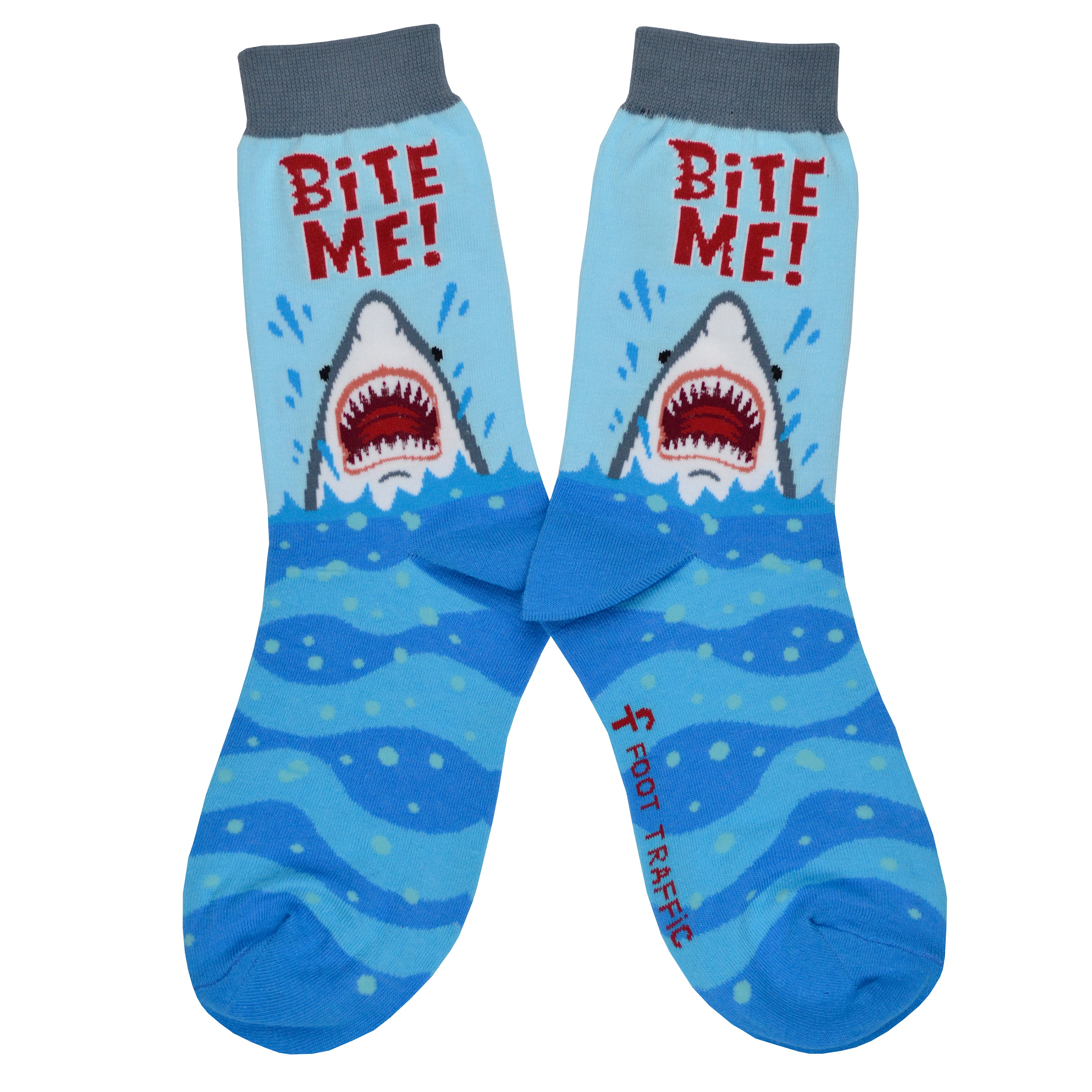 Shown in a flatlay, a pair of women's Foot Traffic brand cotton crew socks in blue with a grey cuff and blue heel and toe. The leg of the sock features a great white shark poised to bite with the words 