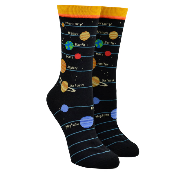 Shown on a leg form, these black cotton women's crew socks with a yellow cuff by the brand Foot Traffic feature the planets and their names Mercury, Venus, Earth, Mars, Jupiter, Saturn, Uranus and Neptune lined up running down the leg of the sock.
