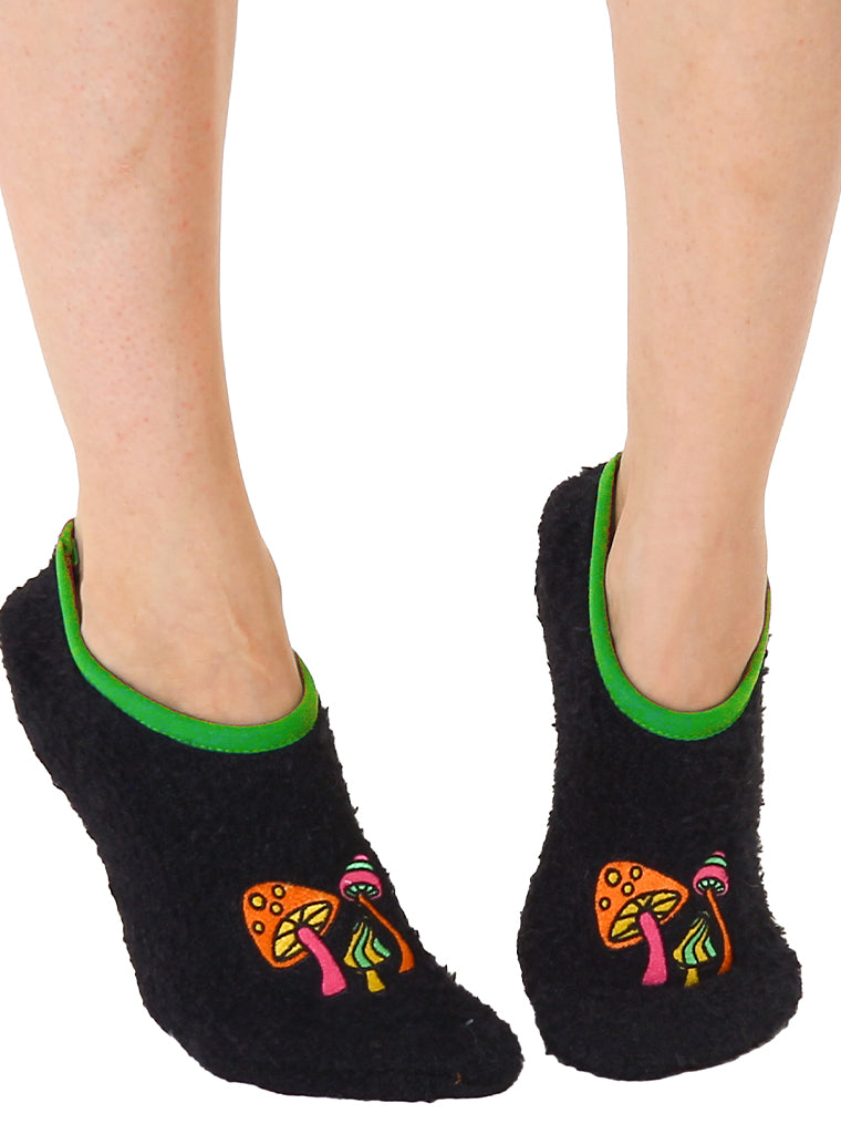 a pair of feet wearing black fuzzy slipper socks with 3 psychedelic mushrooms embroidered on the toes