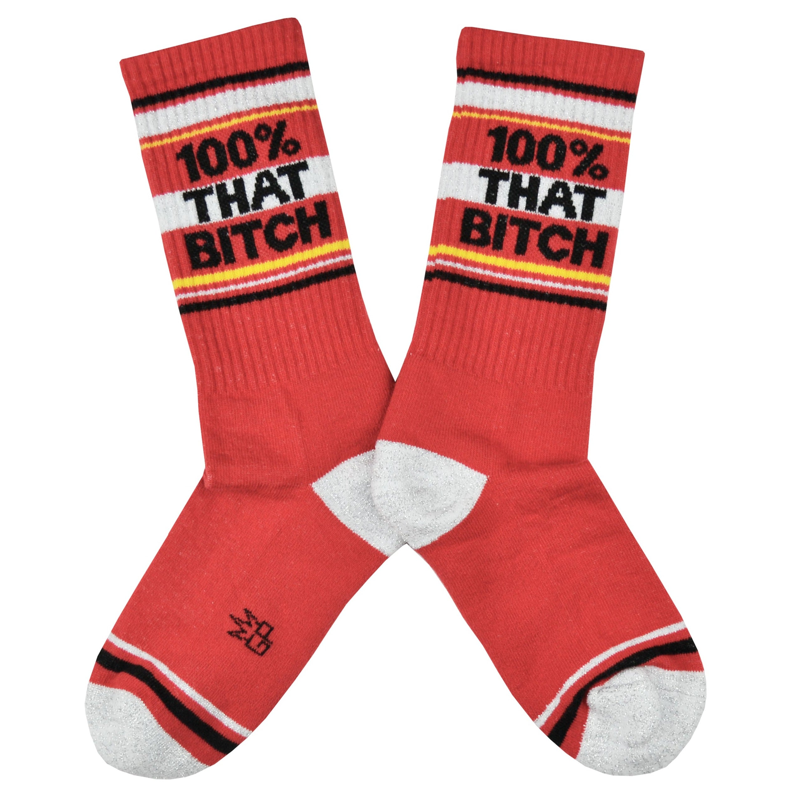 Shown in a flatlay, a pair of cotton crew length unisex Gumball Poodle brand socks in red with a sparkly silver toe and heel. The leg of the sock features, black, sparkly silver, and yellow stripes with the phrase, 