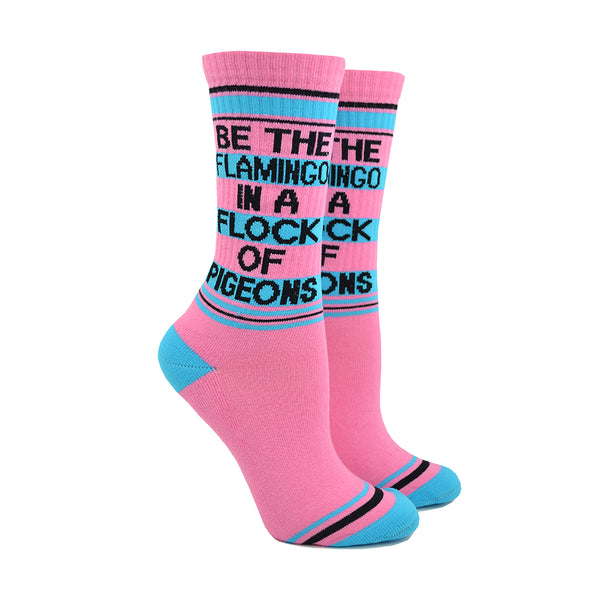 Shown on leg forms, a pair of unisex cotton crew Gumball Poodle brand sock in pink with black and teal stripes around the leg and a teal heel and toe. The text on the sock reads, "BE THE FLAMINO IN A FLOCK OF PIDGEONS".