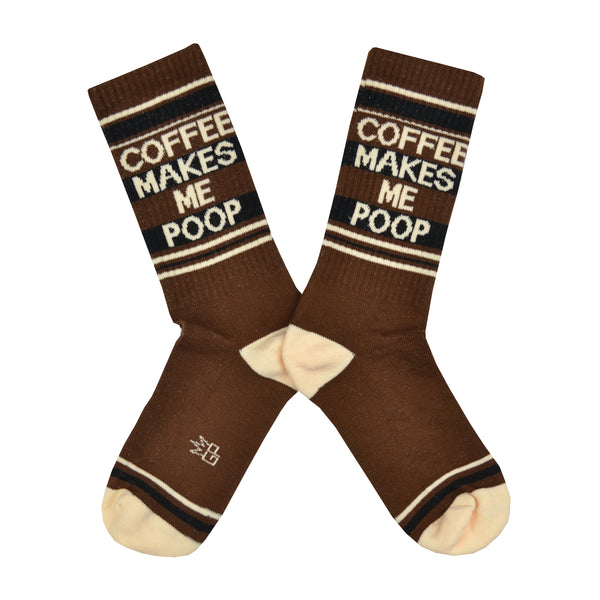 Shown in a flatlay, a pair of Gumball Poodle, dark brown cotton crew socks with tan heel/toe/accent stripes and “Coffee Makes Me Poop” text