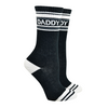 Shown on a foot mold, a pair of Gumball Poodle, black cotton crew socks with white heel/toe/accent stripes and “Daddy” text
