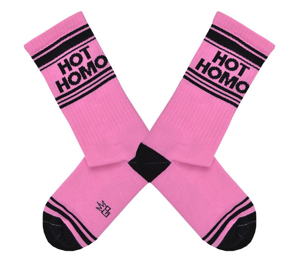 Shown in a flatlay, a pair of pink cotton Gumball Poodle brand unisex crew socks with black striped toe and cuff. These socks feature the words, 