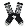 Shown in a flatlay, a pair of black cotton Gumball Poodle brand unisex crew socks with white striped cuff/heel/toe. These socks feature the phrase, "I GIVE THE BEST BLOW JOBS" in alternating black and white font.