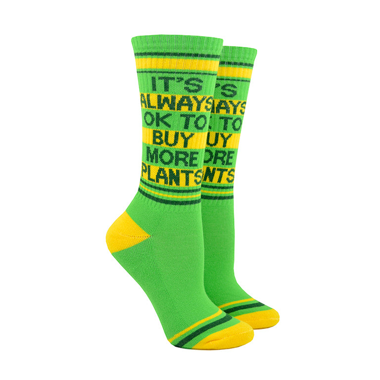 Shown on a foot mold, a pair of Gumball Poodle, lime-green cotton crew socks with yellow heel/toe/accent stripes and dark green “It’s Always Okay to Buy More Plants” text