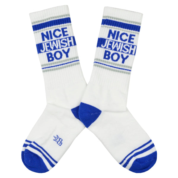 Shown in a flatlay, a pair of Gumball Poodle brand unisex cotton crew sock in white with a blue striped cuff/heel/toe and the words, "NICE JEWISH BOY" on the leg.