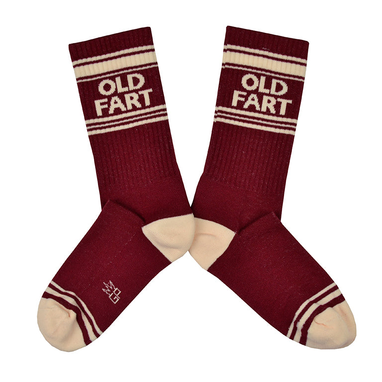 Shown in a flatlay, a pair of Gumball Poodle brand unisex cotton crew sock in maroon with an off-white striped heel/toe/cuff and the words, 