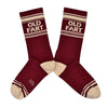 Shown in a flatlay, a pair of Gumball Poodle brand unisex cotton crew sock in maroon with an off-white striped heel/toe/cuff and the words, "OLD FART" on the leg.