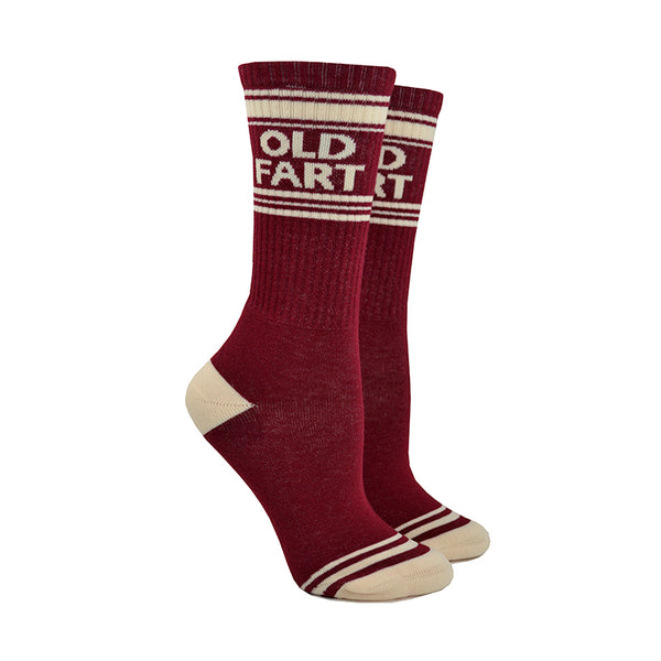 Shown on leg forms, a pair of Gumball Poodle brand unisex cotton crew sock in maroon with an off-white striped heel/toe/cuff and the words, "OLD FART" on the leg.
