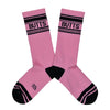 These pink cotton unisex crew socks with a black striped toe and cuff by the brand Gumball Poodle feature the word "BUTTS" on the leg.
