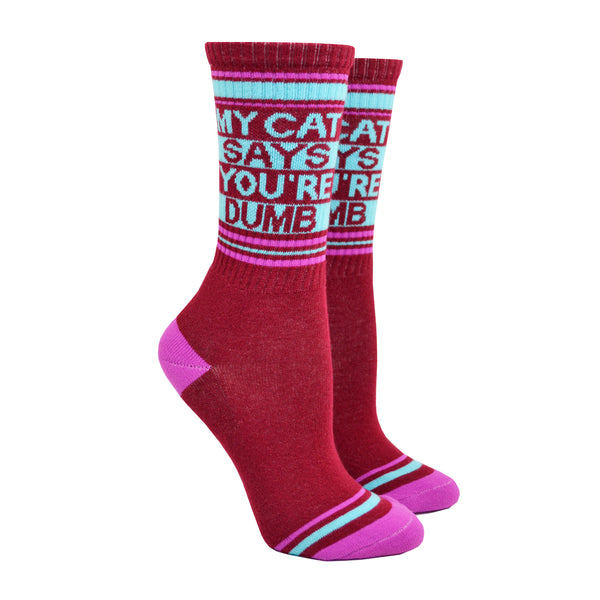 Shown on leg forms, a pair of Gumball Poodle brand unisex cotton crew socks in maroon with a magenta heel/toe and a blue striped cuff that says, 'MY CAT SAYS YOUR'RE DUMB" on the leg.