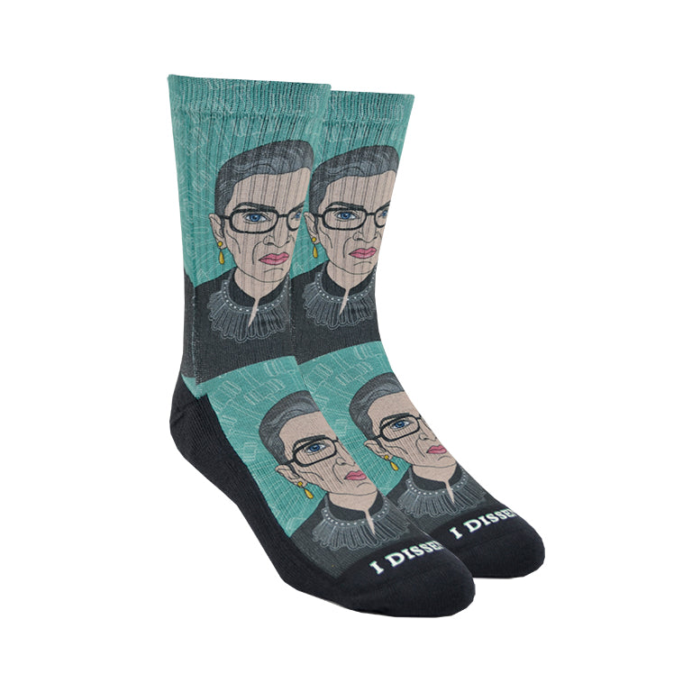 Shown in size large on leg forms, a pair of Good Luck Socks brand unisex green polyester and cotton crews socks. The front of these socks features a caricature of the iconic Supreme Court Justice Ruth Bader Ginsburg in one of her well-known collars with the words 