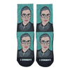 Shown in a flatlay, a pair of Good Luck Socks brand unisex green polyester and cotton crew socks. The front of these socks features a caricature of the iconic Supreme Court Justice Ruth Bader Ginsburg in one of her well-known collars with the words "I dissent!" printing on the black toe of the sock.