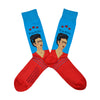 Shown in a flatlay, a pair of Hot Sox cotton men’s crew socks with the artist Frida Kahlo in a red shirt with a blue background and her name in text above her