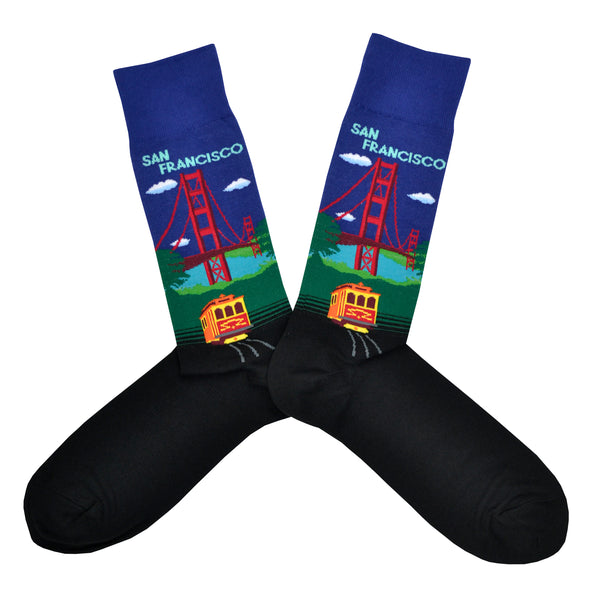 Shown in a flatlay, a pair of Hot Sox cotton men’s crew socks with Golden Gate Bridge, hills, trolley and navy blue sky