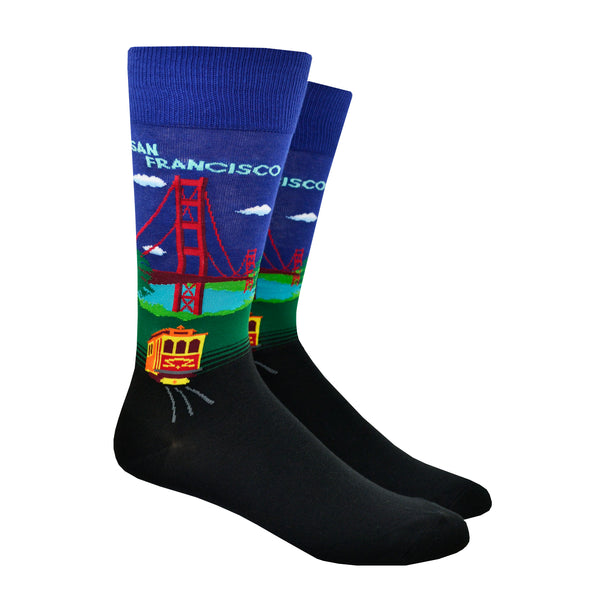 Shown on a leg form, a pair of Hot Sox cotton men’s crew socks with Golden Gate Bridge, hills, trolley and navy blue sky
