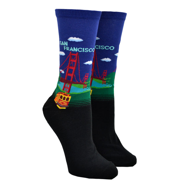 Shown on a leg form, a pair of Hot Sox cotton women’s crew socks with Golden Gate Bridge, hills, trolley and navy blue sky