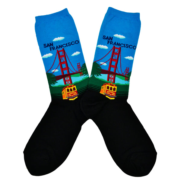 Shown in a flatlay, a pair of Hot Sox cotton women’s crew socks with Golden Gate Bridge, hills, trolley and light blue sky