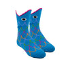 Shown on leg forms, a pair of K.Bell brand kids cotton crew socks in blue. The sock features a mouth shaped top with a cartoon eye and rainbow scale details on the whole sock.