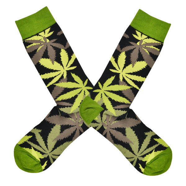 Shown in a flatlay, a pair of men's crew length K.Bell brand nylon and cotton socks in black with a bright green heel, toe, and cuff. The sock features an all over motif of marijuana leaves in shades of green and brown.