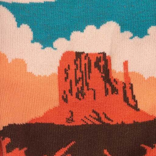 A close up of the stitching on a pair of Sock it to Me cotton socks, showing a cloudy sky and a desert mesa in oranges and blues