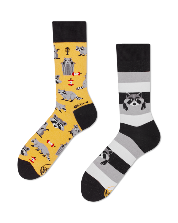 flatlay of a pair of mistmatched crew length socks, one yellow with a pattern of raccoons, trash cans, apple cores, fish bones and raccoon faces, the other shaes of black and gray stripes with a couple raccoons appearing to crawl out of the stripes