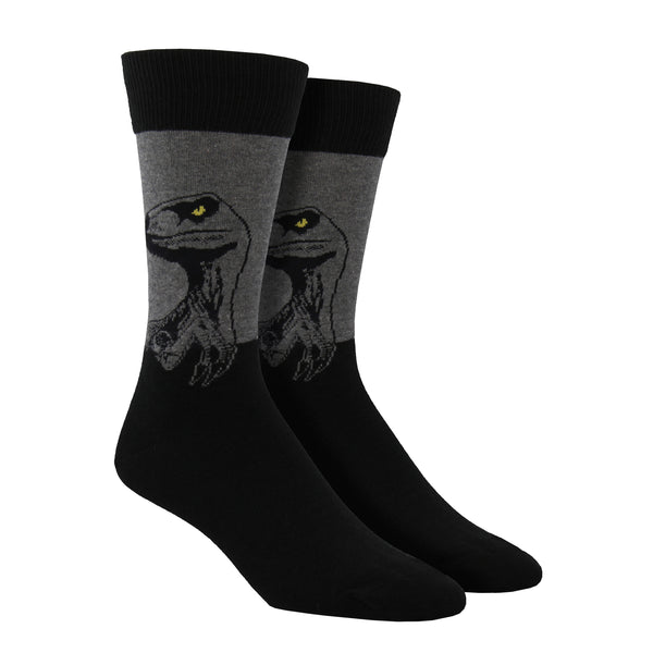 Shown on a foot form, a pair of Socksmith's black cotton men's crew socks with gray raptor dinosaur head design